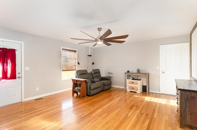 living room with ceiling fan, visible vents, baseboards, and light wood-style flooring