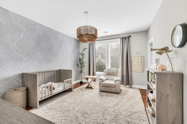 bedroom with visible vents, an accent wall, wood finished floors, baseboards, and wallpapered walls