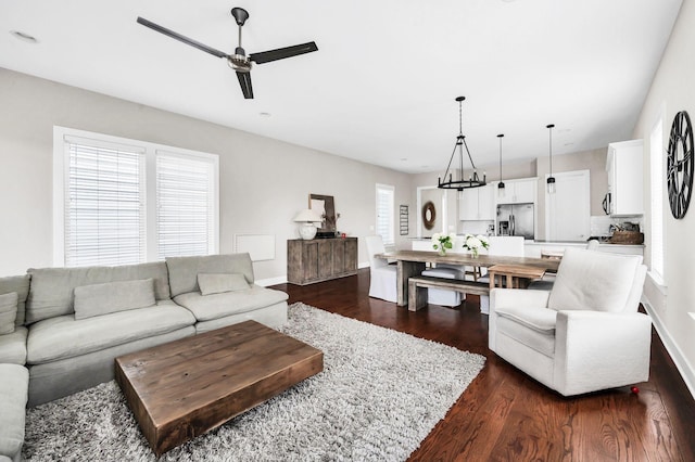 living room with a healthy amount of sunlight, dark wood-style floors, baseboards, and ceiling fan with notable chandelier