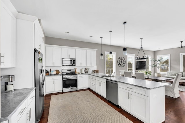 kitchen featuring dark wood-style floors, appliances with stainless steel finishes, open floor plan, a sink, and a peninsula