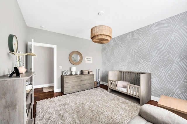 bedroom with an accent wall, dark wood-type flooring, baseboards, and wallpapered walls