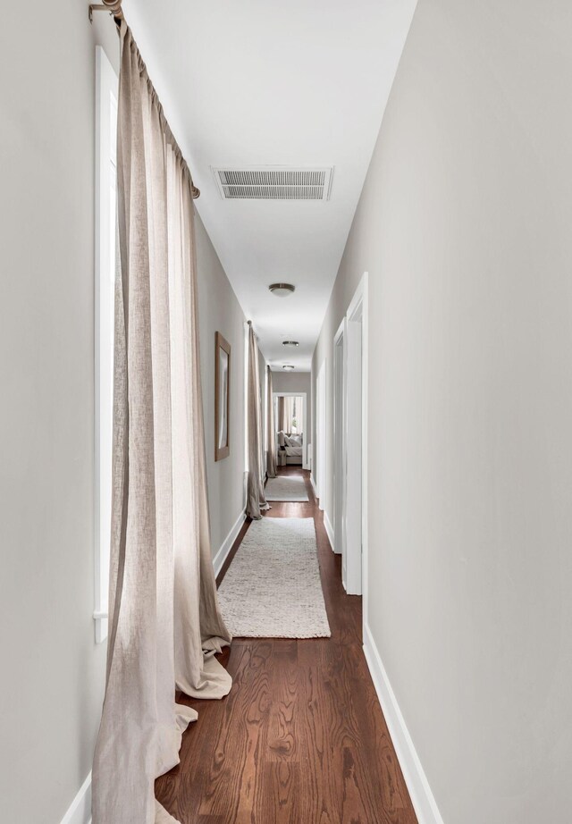 hallway with dark wood-style flooring, visible vents, and baseboards