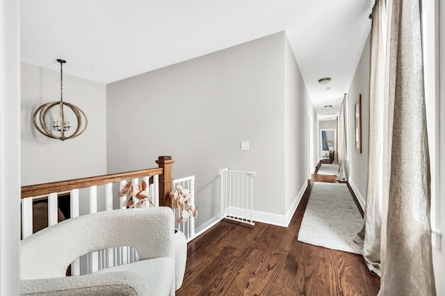 corridor with an inviting chandelier, wood finished floors, an upstairs landing, and baseboards