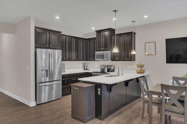 kitchen with dark wood finished floors, stainless steel appliances, hanging light fixtures, a sink, and a peninsula