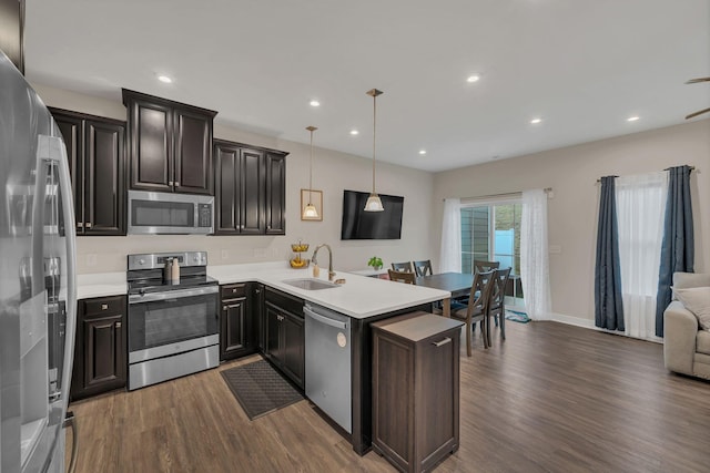 kitchen with open floor plan, dark wood-style flooring, a peninsula, stainless steel appliances, and a sink