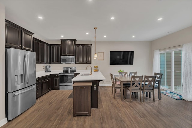 kitchen with stainless steel appliances, dark wood-type flooring, a sink, light countertops, and a kitchen bar