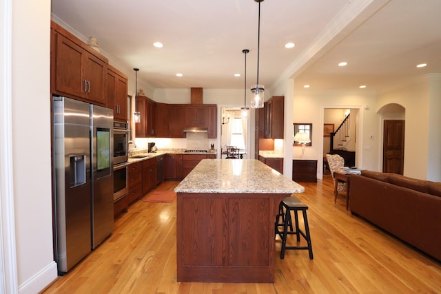 kitchen featuring a breakfast bar, under cabinet range hood, a center island, light wood-style floors, and appliances with stainless steel finishes