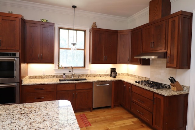 kitchen featuring crown molding, under cabinet range hood, light wood-style floors, stainless steel appliances, and a sink