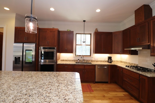 kitchen with a sink, under cabinet range hood, appliances with stainless steel finishes, crown molding, and light wood-type flooring