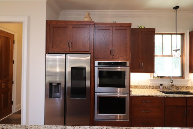 kitchen featuring a sink, decorative light fixtures, stainless steel appliances, crown molding, and light stone countertops