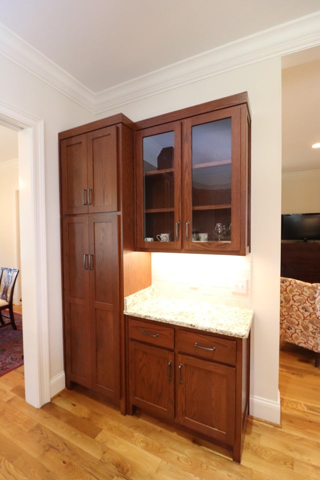 interior space featuring light wood finished floors, glass insert cabinets, crown molding, and light stone countertops