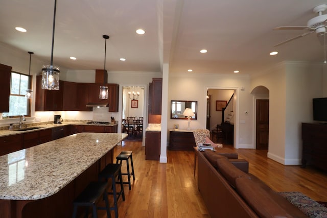 kitchen featuring a breakfast bar, light wood-style floors, gas stovetop, a ceiling fan, and a sink