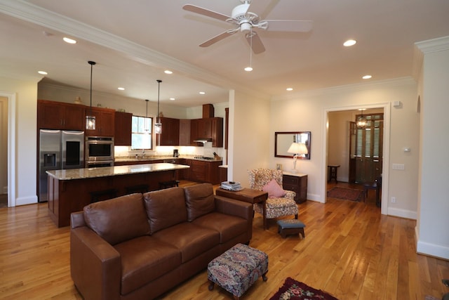 living area with a ceiling fan, baseboards, light wood finished floors, recessed lighting, and ornamental molding