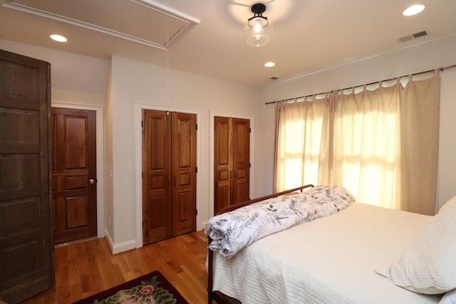 bedroom with wood finished floors, visible vents, attic access, recessed lighting, and multiple closets