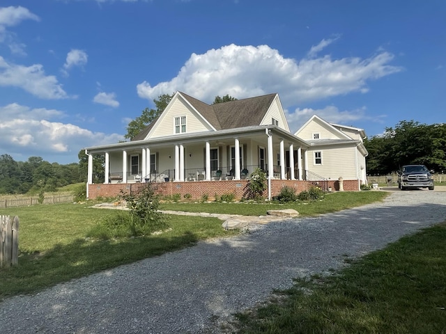 farmhouse with gravel driveway, a porch, a front yard, and fence