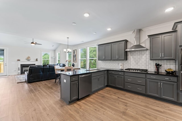 kitchen with a peninsula, a fireplace, wall chimney range hood, appliances with stainless steel finishes, and decorative backsplash