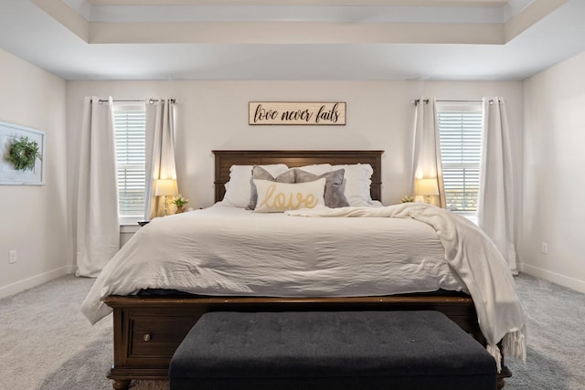 carpeted bedroom featuring baseboards, multiple windows, and a tray ceiling