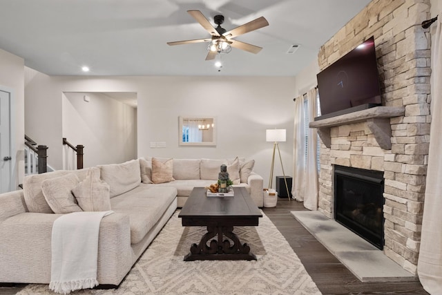 living room featuring visible vents, dark wood finished floors, a stone fireplace, and ceiling fan