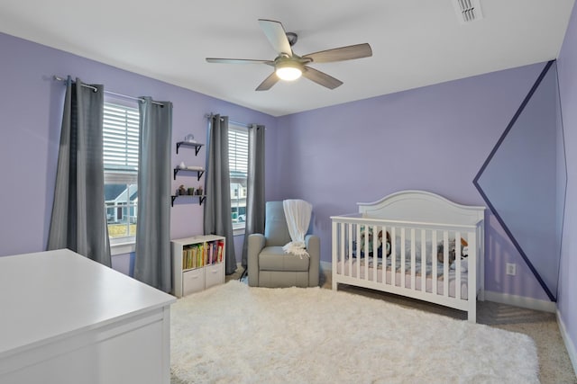 carpeted bedroom with a ceiling fan, visible vents, a crib, and baseboards