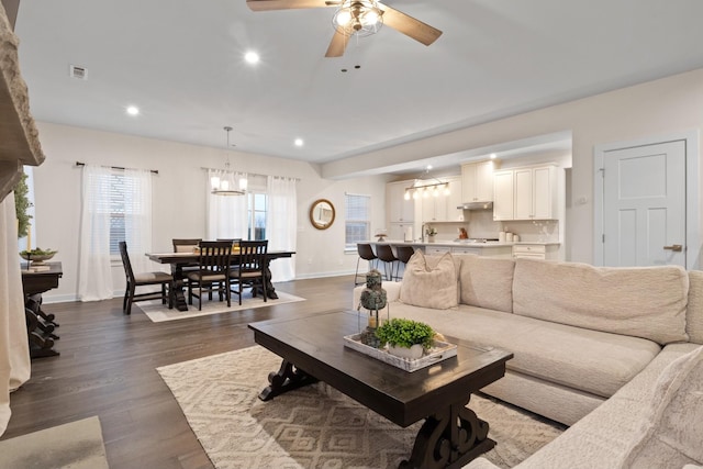 living room featuring recessed lighting, ceiling fan with notable chandelier, dark wood-style flooring, visible vents, and baseboards