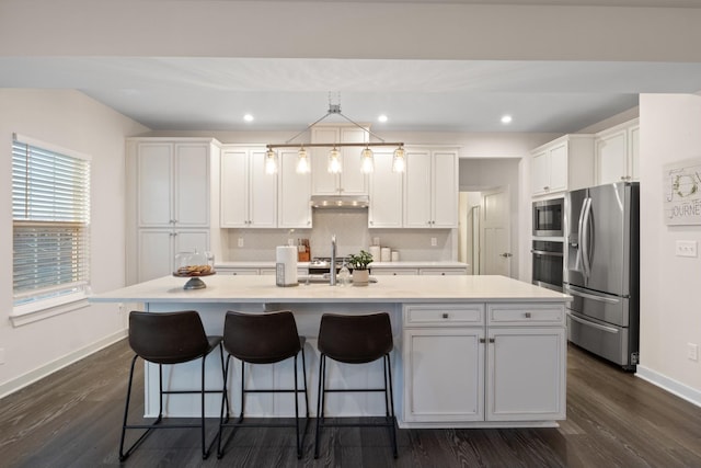 kitchen featuring light countertops, appliances with stainless steel finishes, white cabinetry, an island with sink, and under cabinet range hood