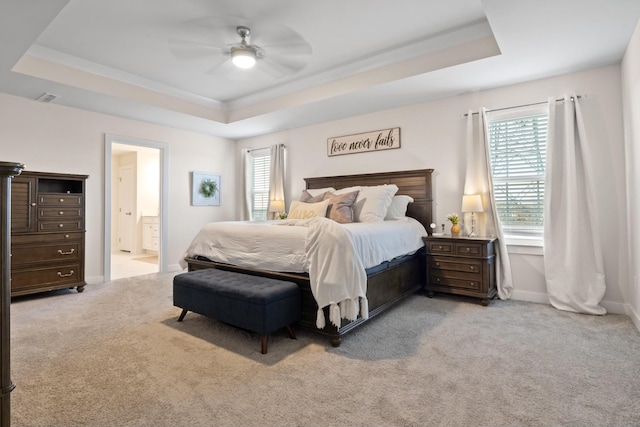 bedroom with light carpet, visible vents, baseboards, a raised ceiling, and ensuite bathroom