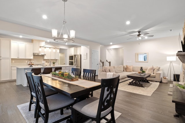 dining area with dark wood-type flooring, recessed lighting, a fireplace, and ceiling fan with notable chandelier