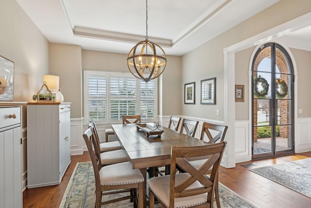 dining space with an inviting chandelier, a raised ceiling, dark wood-type flooring, and wainscoting