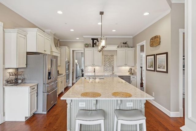 kitchen with an island with sink, dark wood-style floors, ornamental molding, a kitchen breakfast bar, and a sink