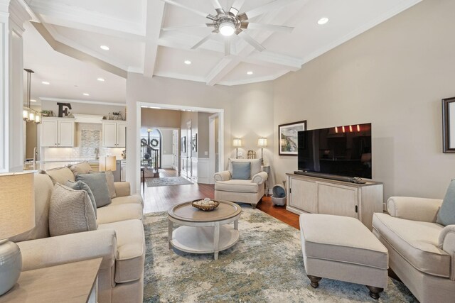 living room with beam ceiling, coffered ceiling, crown molding, and wood finished floors