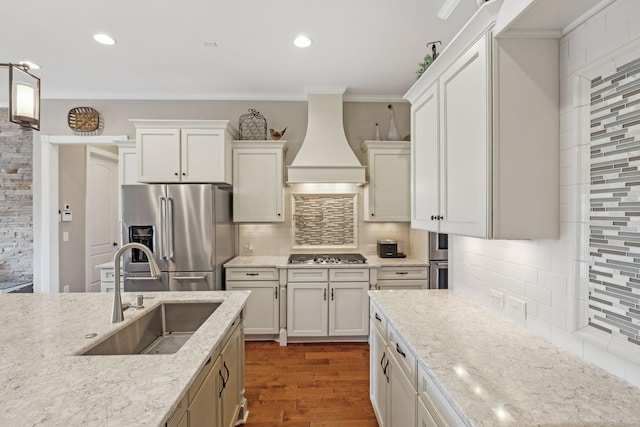 kitchen featuring light stone counters, a sink, custom range hood, appliances with stainless steel finishes, and crown molding