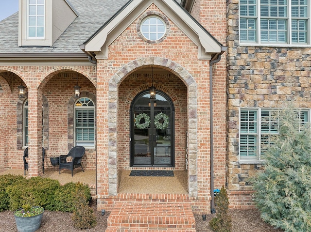 property entrance featuring stone siding, roof with shingles, and brick siding