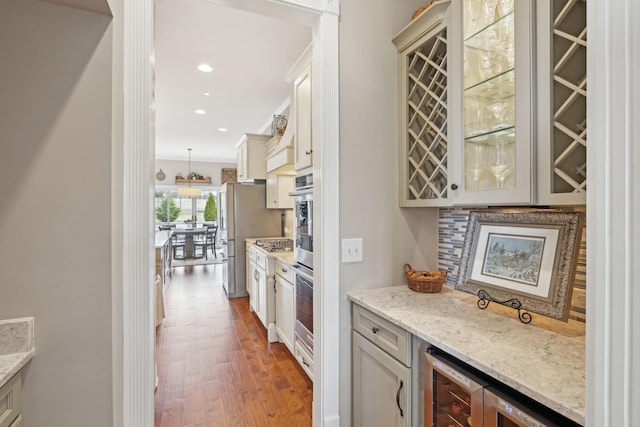 bar with a dry bar, tasteful backsplash, appliances with stainless steel finishes, wood finished floors, and recessed lighting