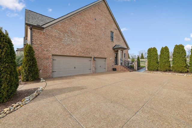 view of side of property featuring driveway, a shingled roof, a garage, and brick siding