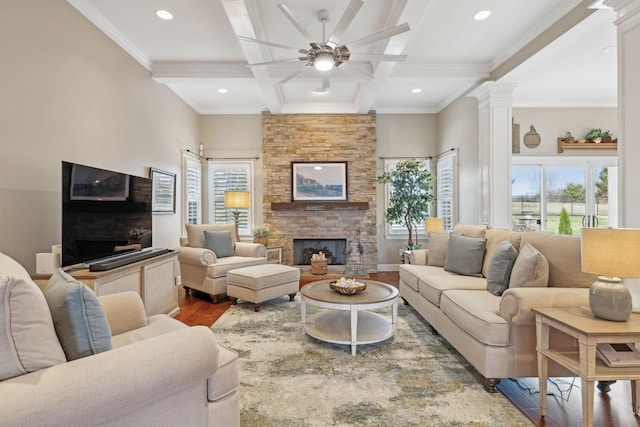 living area with a stone fireplace, wood finished floors, coffered ceiling, beamed ceiling, and ornate columns