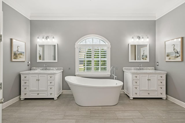 full bath featuring a soaking tub, two vanities, crown molding, and baseboards