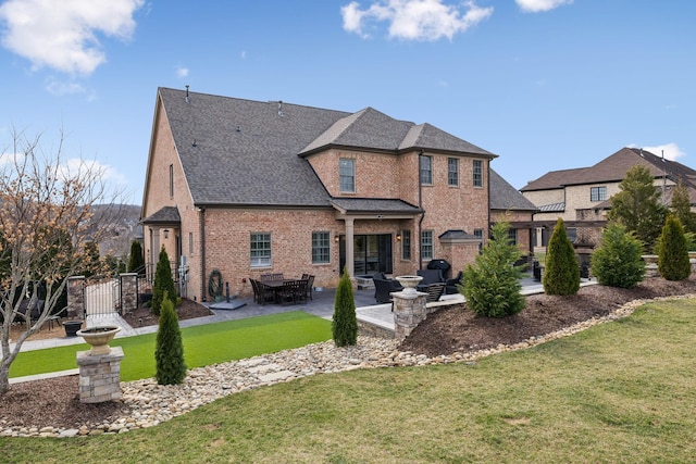 rear view of house with brick siding, a shingled roof, a lawn, a patio area, and fence