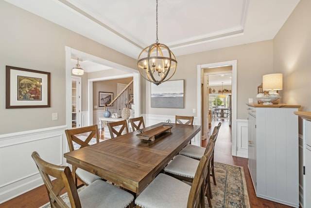 dining area featuring a raised ceiling, wainscoting, stairway, dark wood-style flooring, and an inviting chandelier