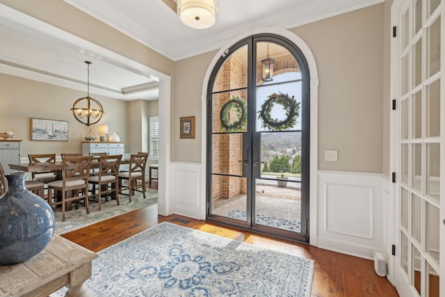 entrance foyer featuring french doors, a wainscoted wall, a notable chandelier, ornamental molding, and hardwood / wood-style floors