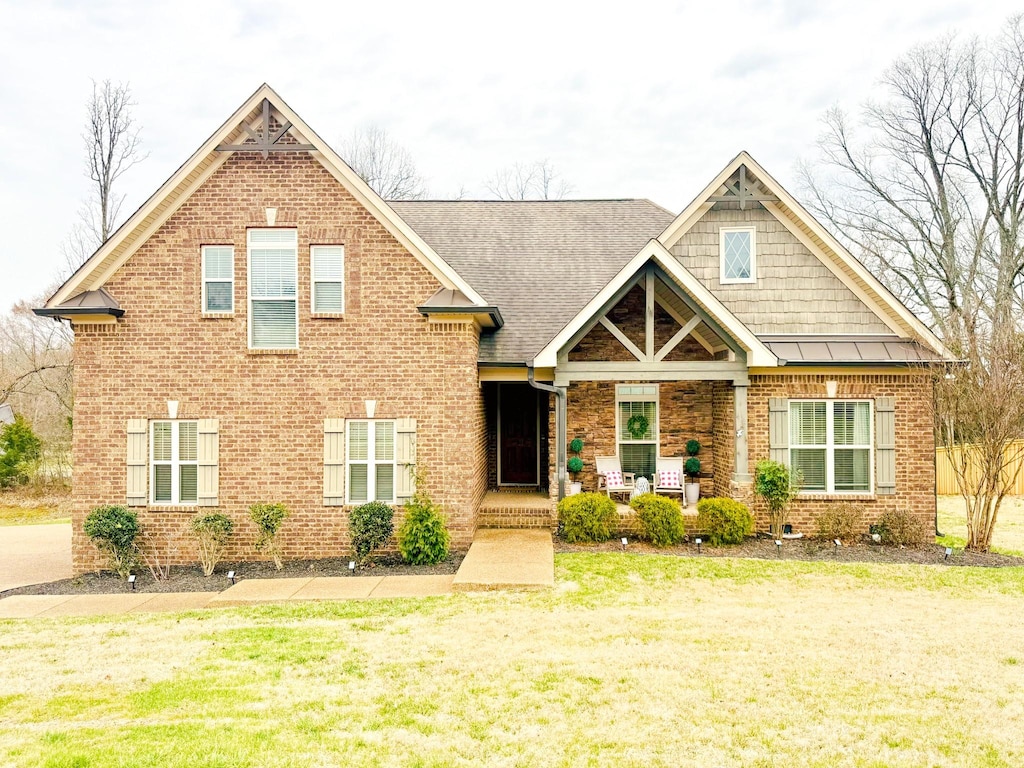 craftsman house featuring a porch, a front yard, a standing seam roof, and brick siding