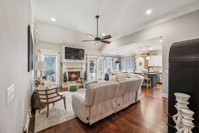 living area with dark wood-style floors, recessed lighting, a tiled fireplace, and lofted ceiling