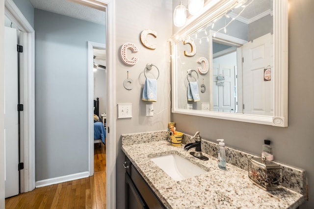 ensuite bathroom with baseboards, connected bathroom, wood finished floors, a textured ceiling, and vanity