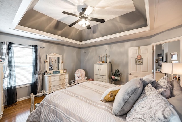 bedroom featuring a ceiling fan, a raised ceiling, baseboards, and wood finished floors