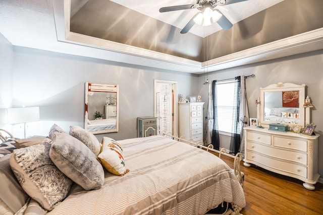 bedroom with a ceiling fan, a raised ceiling, and wood finished floors