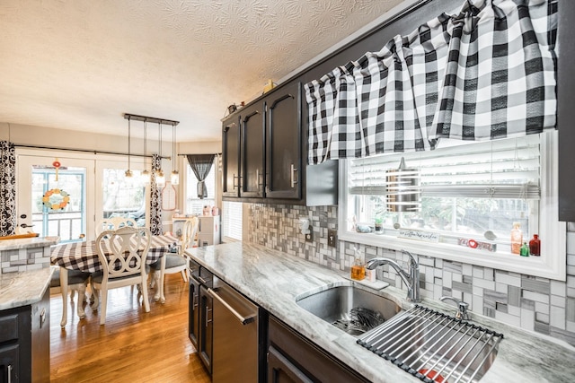 kitchen with light wood finished floors, tasteful backsplash, dishwasher, light stone counters, and a sink