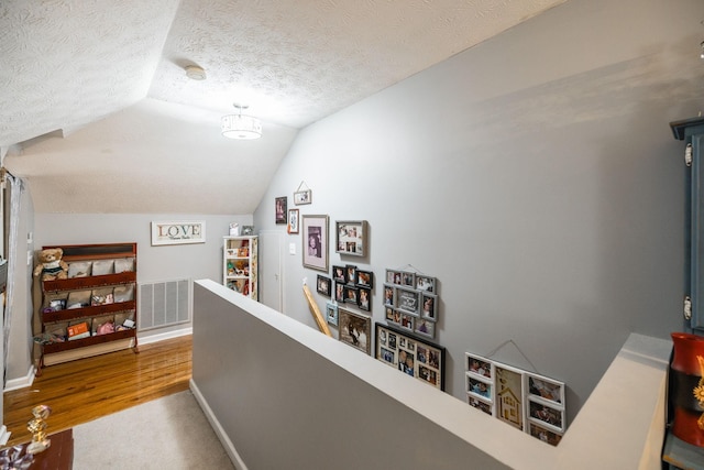 hallway featuring visible vents, vaulted ceiling, a textured ceiling, an upstairs landing, and baseboards