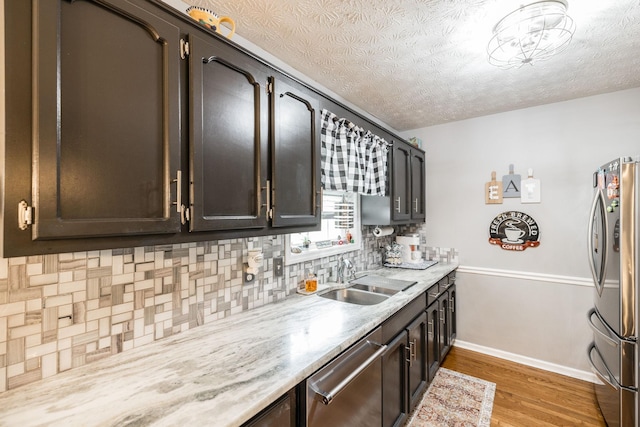 kitchen with baseboards, decorative backsplash, appliances with stainless steel finishes, light wood-type flooring, and a sink