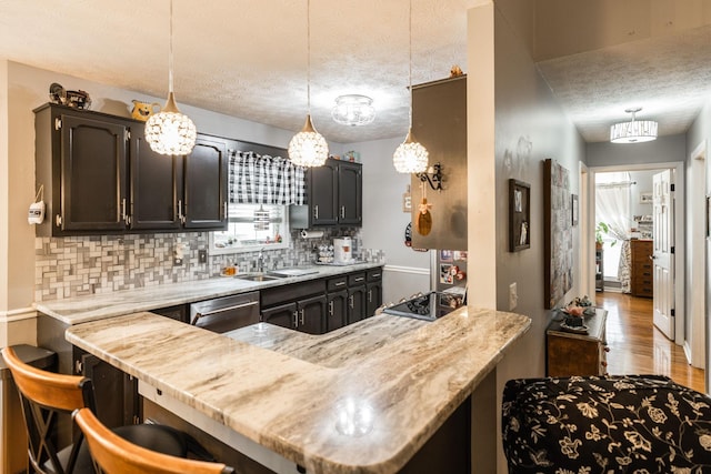 kitchen featuring a textured ceiling, a peninsula, a sink, stainless steel dishwasher, and decorative backsplash