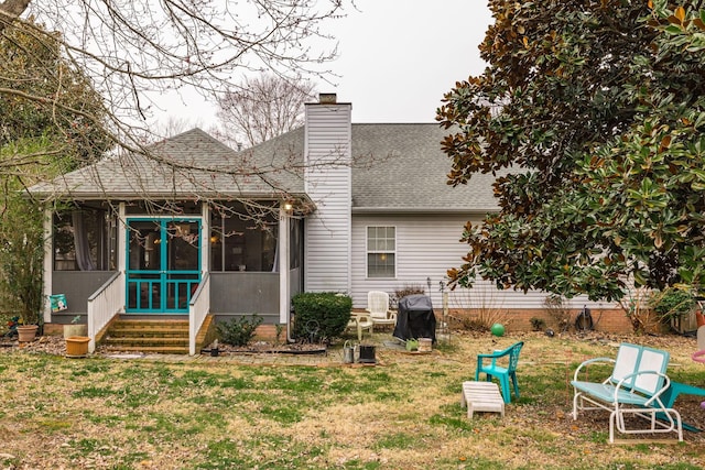 rear view of property featuring a sunroom, roof with shingles, a lawn, and a chimney