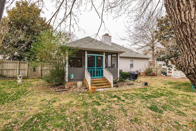 rear view of house featuring a fenced backyard, a sunroom, roof with shingles, a lawn, and a chimney